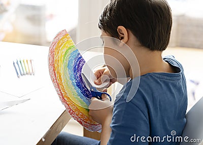 Kid is isolation using scissors cutting paper in rainbow shape on white background, Children activities at home while school off. Stock Photo