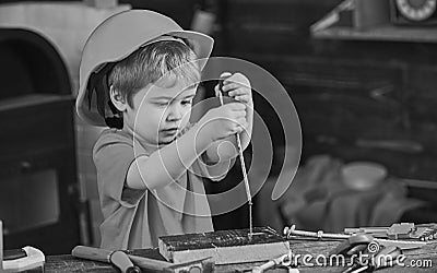 Kid learning to use screwdriver. Concentrated kid in orange helmet working in workshop. Future occupation concept Stock Photo