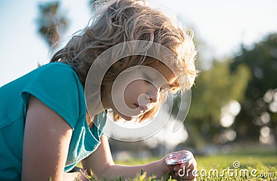 Kid with magnifying glass lying in grass. Happy smiling child boy relaxing on the grass. Cute kid boy enjoying on grass Stock Photo