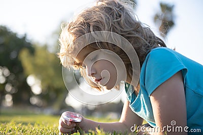 Kid with magnifying glass lying in grass. Happy smiling child boy relaxing on the grass. Cute kid boy enjoying on grass Stock Photo