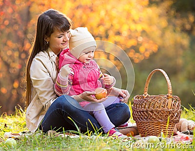 Kid and mother sit with apples basket outdoors in autumnal park Stock Photo