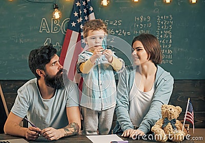 Kid with parents in classroom with usa flag, chalkboard on background. American family sit at desk with son. Patriotic Stock Photo