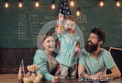 Kid with parents in classroom with usa flag, chalkboard on background. Patriotic education concept. American family sit Stock Photo