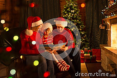 Kid with parents read stories sitting on coach in front of fireplace in Christmas decorated house interior Stock Photo