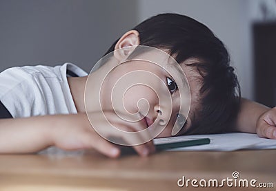 Kid playing colour pencil sitting alone and looking down with bored face, Preschool child boy laying head down on table looking Stock Photo