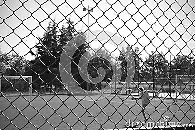 Kid playing football on a playground in a park surrounded by a wire mesh. in black and white for greater drama. alone on the footb Stock Photo