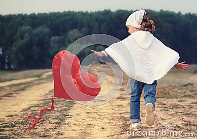 Kid girl playing with a red heart kite Stock Photo