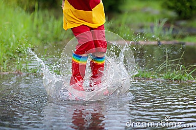 Kid playing out in the rain. Children with umbrella and rain boots play outdoors in heavy rain. Little boy jumping in muddy puddle Stock Photo