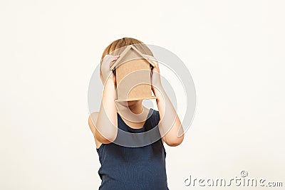Kid playing with toys house. Little child hid his face behind a small house. Child holding small house, and dreaming about his own Stock Photo