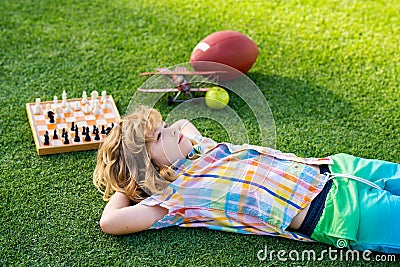 Kid relax in park, laying on grass, daydreaming. Board game in backyard, laying on grass. Stock Photo