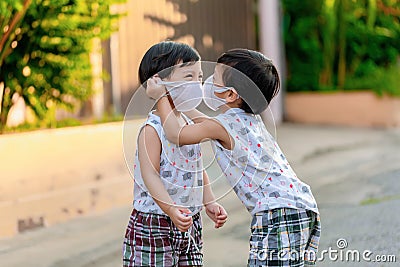 Kid in safety wearing mask in town. Twin Children wearing medical face mask outdoor. Twin Child helps to put a mask on his face t Stock Photo