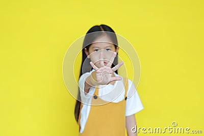 Kid show warning expression isolated on yellow background. Asian little girl doing stop sing with palm of hand. Selective focus at Stock Photo