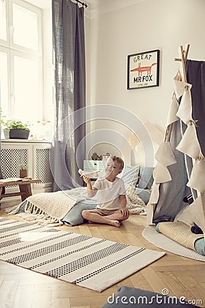 Kid sitting on the floor with toy airplane in natural playroom with comfortable bed and scandinavian tent, real photo Stock Photo