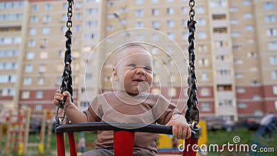The kid on a swing for the first time in his life gets a lot of fun. Little kid swinging alone in park. The little boy Stock Photo