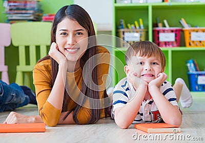 Kid and teacher looking at camera and smile lying down at school library. floor.kindergarden learning school Stock Photo