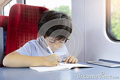 Kid traveling by the train, Child drawing or watching cartoon on teblet sitting by the window. Little boy in a high speed express Stock Photo