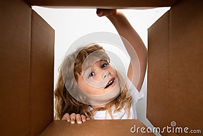 Kid unpacking and opening carton box, and looking inside with surprise face. Unpacking cardboard box for kids. Stock Photo