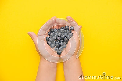 Kid& x27;s palms with a handful of blueberries on a bright yellow background with place for text Stock Photo