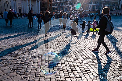 Kids catching and blowing soap bubbles flying on Piazza del Popolo, People Square in Rome full of people, tourists and locals with Editorial Stock Photo