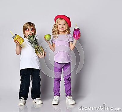 Kids in colorful casual clothes. Smiling, holding yellow and pink cocktail bottles, apple, pineapple. Posing isolated on white Stock Photo