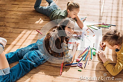 Kids drawing on paper with pencils while lying on floor Stock Photo