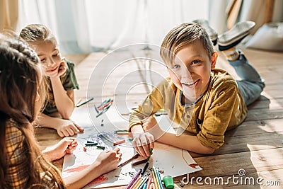 Kids drawing on paper with pencils while lying on floor Stock Photo