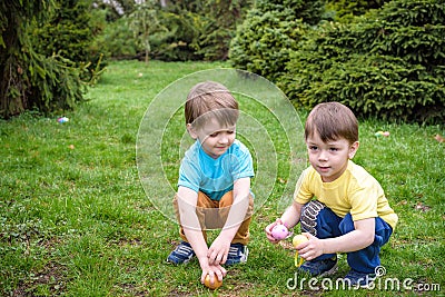 Kids on Easter egg hunt in blooming spring garden. Children searching for colorful eggs in flower meadow. Toddler boy and his brot Stock Photo