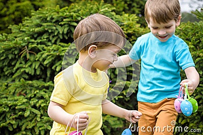 Kids on Easter egg hunt in blooming spring garden. Children searching for colorful eggs in flower meadow. Toddler boy and his brot Stock Photo