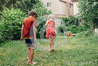 Kids friends splashing with gardening hose sprinkler on backyard on summer day. Stock Photo