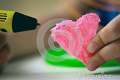 Kids hand holding yellow 3D printing pen with filaments and makes heart on white background. Top view. Copy space for Stock Photo