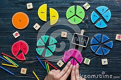 Kids hand moves colorful math fractions on dark wooden background or table. Interesting creative funny math for kids Stock Photo