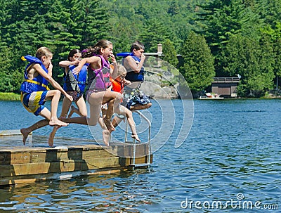 Kids having summer fun jumping off dock into lake Stock Photo