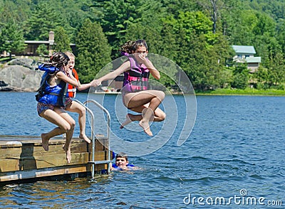 Kids having summer fun jumping off dock into lake Stock Photo