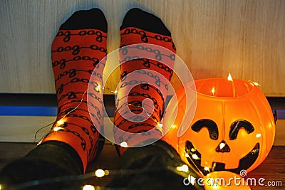 Kids legs in stylish warm bright colorful striped funny socks in garland lights on floor with pumpkins in room. Stock Photo