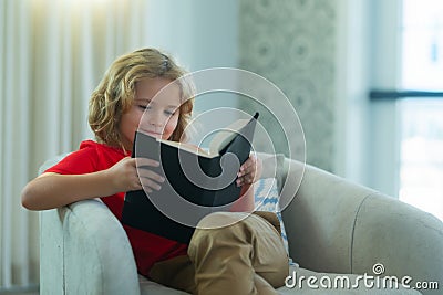 Kids and literature. Child reading book, sitting at home in cozy living room on couch. Concept of education, childhood Stock Photo