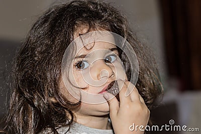 Close-up portrait of a little girl with curly hair. The child eats chocolate candy. Stock Photo