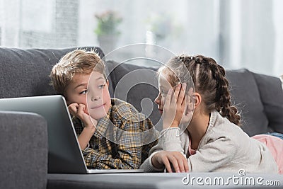Preschooler children lying on a sofa with a laptop and looking at each Stock Photo
