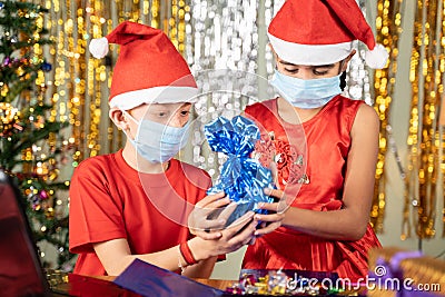 Kids in medical mask in front of laptop Opening gift at home with decorated background during Christmas eve - concept of distant Stock Photo