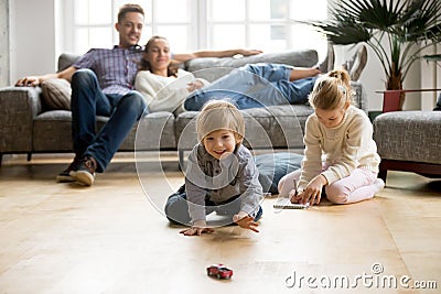 Kids playing on floor, parents relaxing on sofa at home Stock Photo