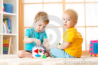 Kids playing with logical toy on soft carpet in nursery roomor kindergarten. Children arranging and sorting shapes or sizes. Stock Photo