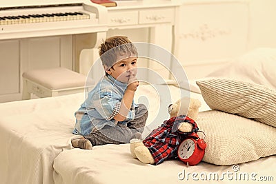 Kids playing with toys. Child in bedroom with silence gesture. Kid put plush bear near pillows and alarm clock, luxury Stock Photo
