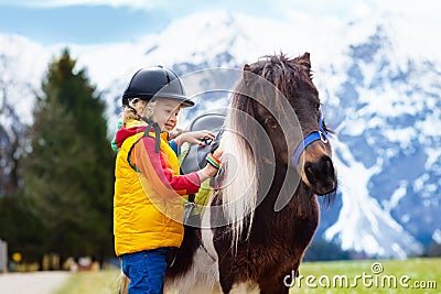 Kids riding pony. Child on horse in Alps mountains Stock Photo