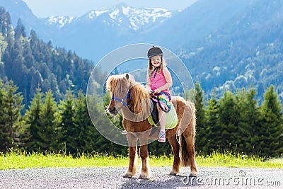 Kids riding pony. Child on horse in Alps mountains Stock Photo