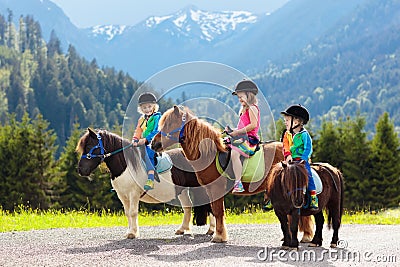 Kids riding pony. Child on horse in Alps mountains Stock Photo