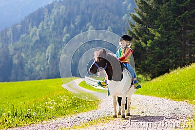 Kids riding pony. Child on horse in Alps mountains Stock Photo