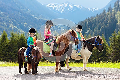 Kids riding pony. Child on horse in Alps mountains Stock Photo