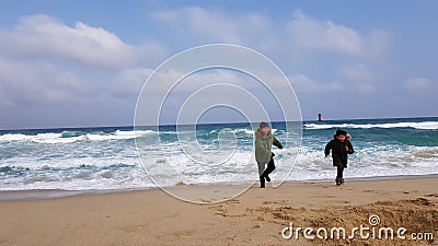 Kids running away from sea waves in winter jackets Editorial Stock Photo