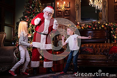 Kids and Santa Claus listening music and dancing at home near the Christmas tree. Family holiday sister and brother Stock Photo