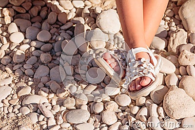 Kids summer sandals. baby shoes on stones beach. girl white fashion footwear, leather sandal ,moccasins.legs of Stock Photo