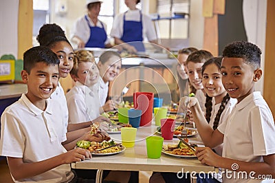 Kids at a table in a primary school cafeteria look to camera Stock Photo